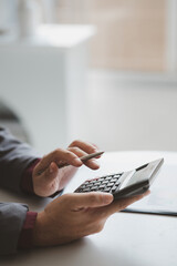 Businessman using a calculator to calculate numbers on a company's financial documents, he is analyzing historical financial data to plan how to grow the company. Financial concept.
