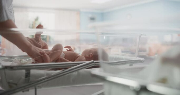 Attentive Mother Changing Diaper to a Newborn Baby. Neonate Child Lying in a Hospital Crib in a Nursery Clinic Facility. Motherhood, Childhood and Medical Concept