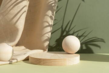 Wooden cylindrical podium, pedestal on a green background with beige curtain and a shadow of palm leaves. Scene for the presentation of a cosmetic product. Empty showcase.