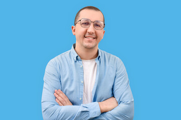 Portrait of a confident young man in a denim shirt with crossed arms looking at the camera on a blue background.