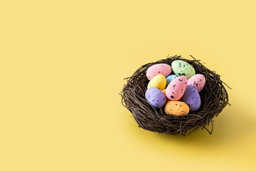 Colorful Easter eggs inside a nest on yellow background. Copy space