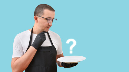 A cook in an apron with a plate in his hands thought about the dish on a blue background. The concept of cooking