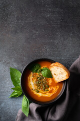 Pumpkin soup with bread, seeds and basil leaf on dark background