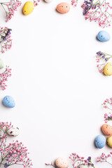Overhead shot of Easter composition with spring flowers and colorful quail eggs over white background. Springtime and Easter holiday concept with copy space. Top view