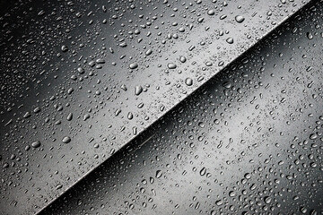 Detail einer silbernen Fahrzeugkarrosserie, bedeckt mit abperlenden Wassertropfen.