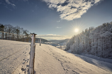 Winterlandschaft im aargauischen Fricktal. Sonnenaufgang über dem Wald mit Blick auf das Dorf...
