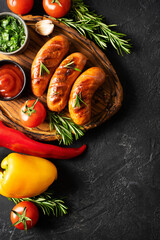 Grill and barbecue sausage on board, with sauce, tomatoes and rosemary on black background