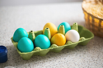 Ready-painted eggs stand on the table with paints and a wicker basket on a sunny day. Easter