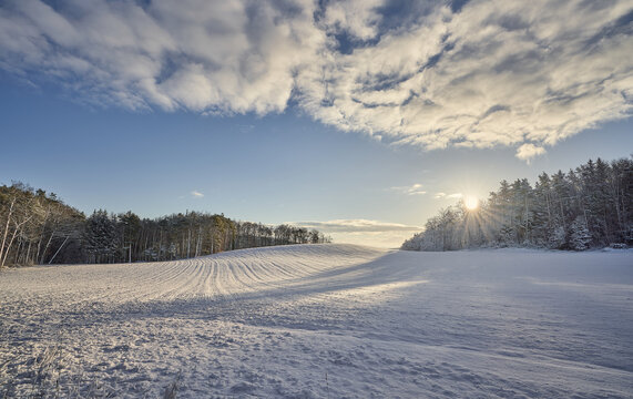 Unber&uuml;hrte Winterlandschaft. Schneebedeckte Felder und ein Sonnenaufgang &uuml;ber dem nahen Wald.