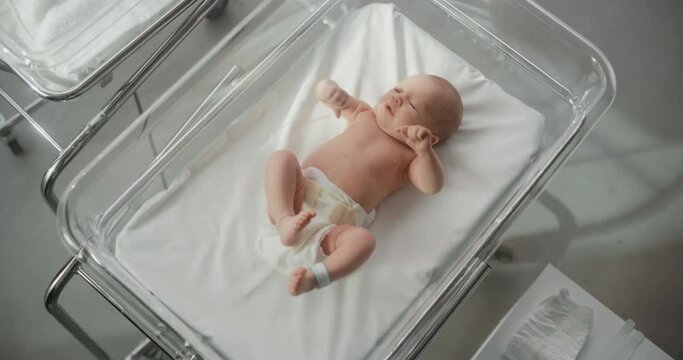 Adorable Small Caucasian Newborn Child Lying in Hospital Bed in a Nursery Clinic. Little Playful and Healthy Baby. Medical Health Care, Maternity and Parenthood Concept. Top Down Portrait