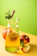Glass carafe of fresh apple juice and organic apples on yellow background. Healthy drink concept with copy space