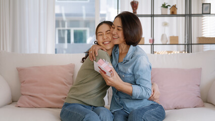 Fototapeta na wymiar May Mother's day young adult grown up child cuddle hug give flower gift box red heart card to mature middle aged mum. Love kiss care mom asia people sitting at home sofa happy smile enjoy family time.