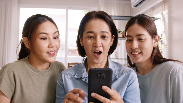 Group Of Asia People Young Adult Child And Middle Aged Mom Looking At Mobile Phone Joy Win Luck Bet Online Game At Home Sofa. Senior Mum Got Lucky Loan Money Sale Reward On Shopping Discount Promotion