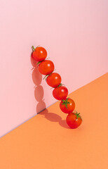 Fresh cherry tomatoes in a row on a pink and orange background. Minimal natural food concept. Creative vegetarian food or diet composition.