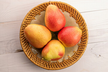 Four ripe yellow-red pears in a ceramic plate on a white wooden table.