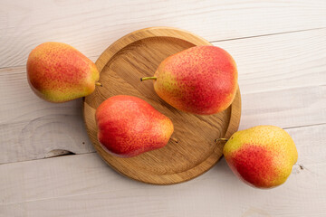 Four ripe yellow-red pears with a round wooden tray, close-up, on a white wooden table, top view.