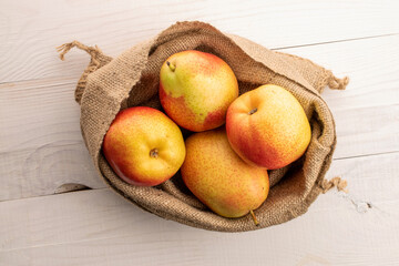 Four ripe yellow-red pears in a jute bag, on a white wooden table, top view.