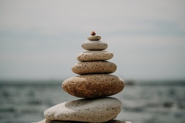 Balanced rock pyramid on sea pebbles beach, at sunset. Golden sea bokeh on background. Selective focus, zen stones on sea beach, meditation, spa, harmony, calm, balance concept
