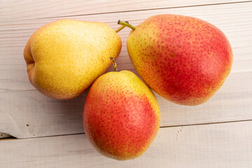 Three organic yellow-red pears, close-up, on a white wood table, top view.