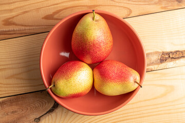 Three ripe yellow-red pears in a ceramic plate, on a wooden table, top view,