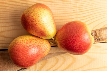 Three organic yellow-red pears, close-up, on a wooden table, top view.