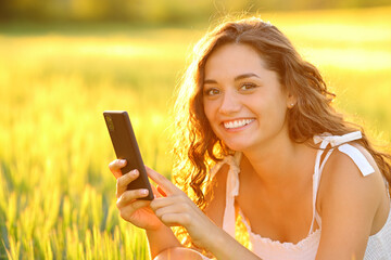 Happy woman posing in a field holding phone