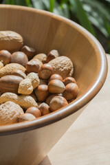 Assorted various nuts in a big wooden bowl against a leafy green background
