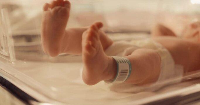 Cute Little Caucasian Newborn Baby Lying in Bassinet in a Maternity Hospital. Portrait of a Tiny Playful and Energetic Child with a Name ID Tag on the Leg. Warm Color Grading