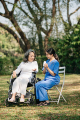 Elderly asian senior woman on wheelchair with Asian careful caregiver and encourage patient, walking in garden. with care from a caregiver and senior health insurance..