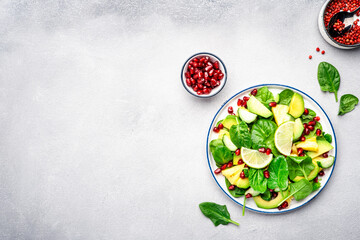 Fresh vegan salad with pineapple, spinach, avocado and pomegranate seeds, gray kitchen table, top...