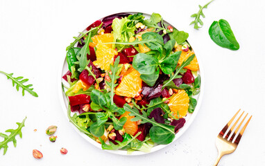 Beet and orange healthy salad with arugula, lamb lettuce, mini chard and pistachios, white kitchen table, copy space. Fresh useful vegan dish for healthy eating