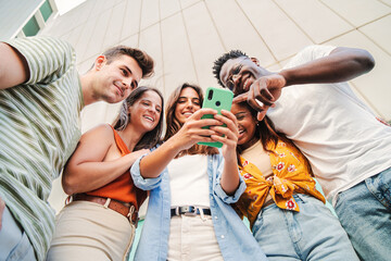 Low angle view of multiracial group of young friends enjoying and smiling using their mobile phone...