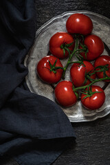 A bunch of tomatoes on a metal vintage plate. Dark background. Top view.