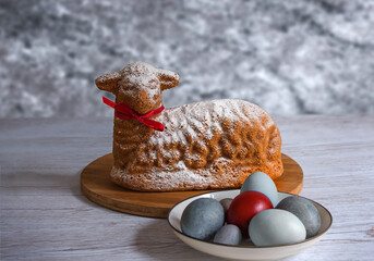 A cupcake in the form of the lamb of God for Easter with a plate of painted eggs against a gray marble wall. Festive treats © Надежда Д