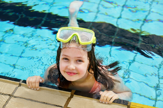Cute happy young girl in goggles swimming and snorking in the swimming pool. Happy child in summer in outdoor pool. Sports and active children.