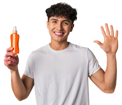A young latin man holding a solar protection cream smiling cheerful showing number five with fingers.