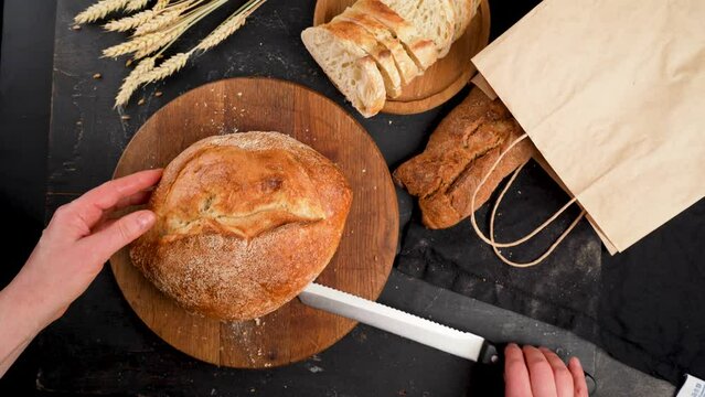 Whole grain bread lies on a kitchen wooden board with a chef holding a cutting knife. Fresh bread on the table close-up. Fresh bread on the kitchen table
