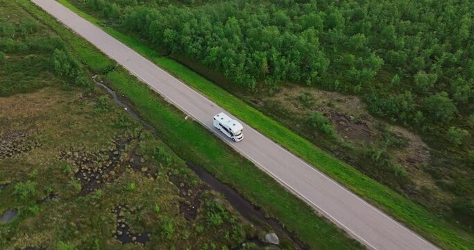 Aerial view around a caravan driving in boreal nature on a summer day - high angle, orbit, drone shot