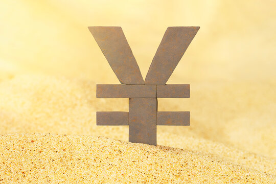 A stone yen sign stands in the sand. Close-up of the national currency symbol. Money rests on the sand. Unstable position of business and finance.