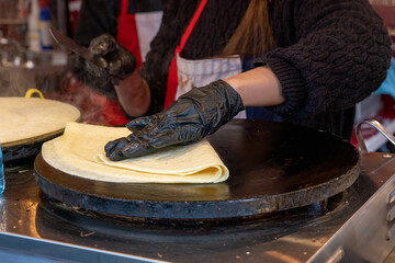 Close-up of a crepe being made on a hotplate. The cook is pressing it down gently to make it...