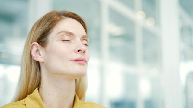 Close up face of serene mature business woman takes a deep breath in the modern glass workplace Calm inspired office worker with closed eyes take break while resting for peaceful mind at light office
