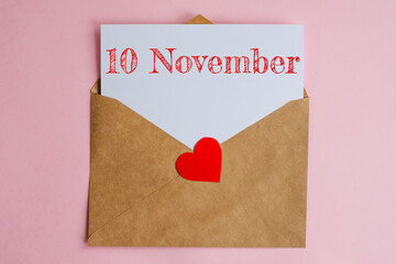 Kraft envelope with a white sheet of paper and a date 10 november, with a red heart. Flat lay on pink background, romance and love concept