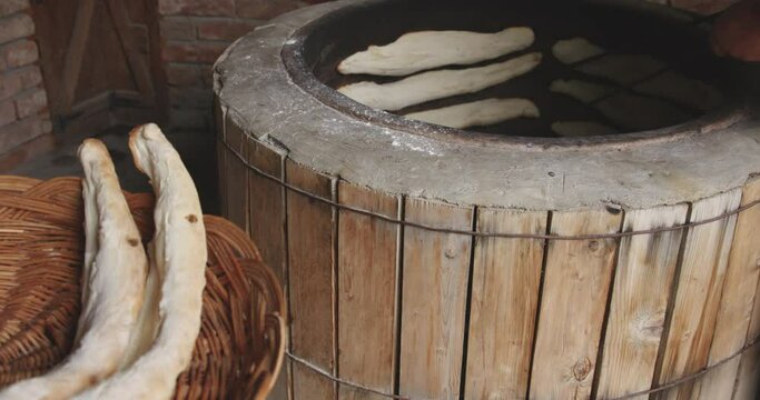 Woman Baker Taking Out The Freshly Baked Shoti Bread From A Round Clay Stove Using An Iron Stick. Kakheti, Georgia - Slow Motion