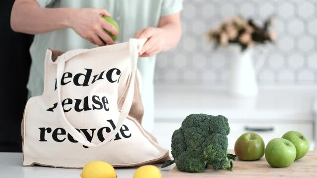 A young woman chooses a zero waste lifestyle. Woman takes out vegetable and fruits from bag after shopping. Waste Reduction and Reducing. Reusable cloth produce bag. Plastic alternatives for food