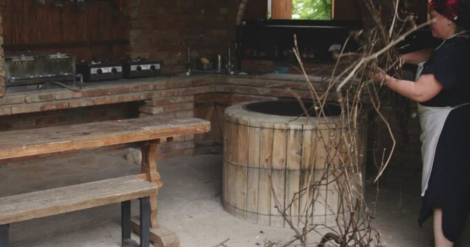 Woman in outdoor brick kitchen adding a pile of branches into a wooden tone.