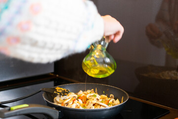 Girl cooking. Girl putting oil in the paella