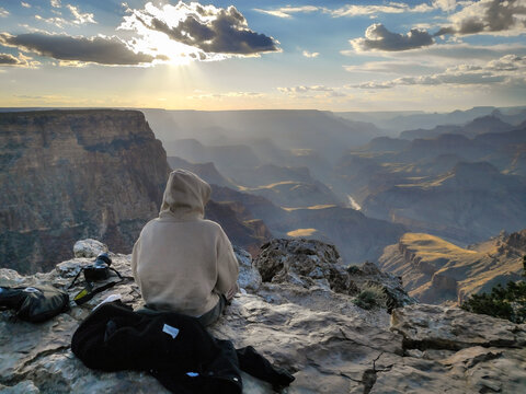 A young girl sitting with her back on the cliff of the grand canyon of colorado taking the cool at dusk