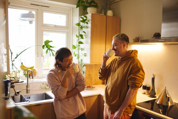 Same Sex Male Couple At Home Talking And Drinking Hot Drinks In Kitchen Together
