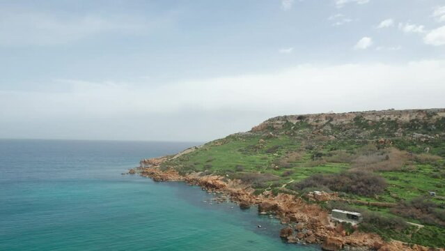 Rotating Aerial View Over An Orange Rocky Shoreline With Turquoise Water At The Base Of A Green Hill, Gozo Island, Malta