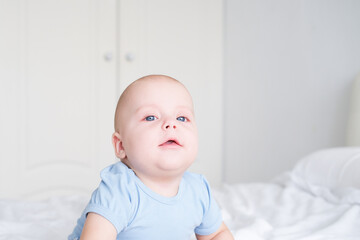 portrait of smiling baby boy with big blue eyes in bodysuit on white bedding. Healthy newborn child